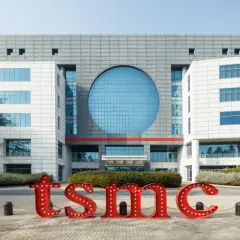 Große rote Buchstaben mit Lichtern bilden "tsmc" vor einem modernen Gebäude. Die TSMC Prognose 2030 wird hier visualisiert.