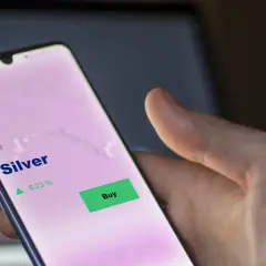 Hand hält Smartphone mit ETF Silber Kursanzeige. Ein grüner "Buy"-Button ist sichtbar, daneben ein Pfeil nach oben und 0,23 %.