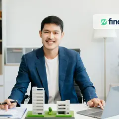 Ein Mann plant seine reits monatliche dividende mit Immobilienmodellen und einem Laptop.