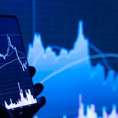 Ein Handy zeigt einen Börsenchart, während im Hintergrund ein größerer Chart zu sehen ist. Ein STP Broker ermöglicht den direkten Marktzugang.