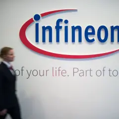 Frau im Anzug geht an Infineon-Logo vorbei. Die Infineon-Aktie Prognose ist ein Thema für Investoren.