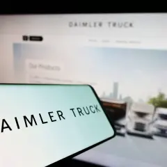 Daimler Truck Logo auf einem Smartphone, im Hintergrund ein Bildschirm mit LKW-Bildern und der Aufschrift "Our Products". Die Daimler Truck Aktie Kurs Prognose im Fokus.