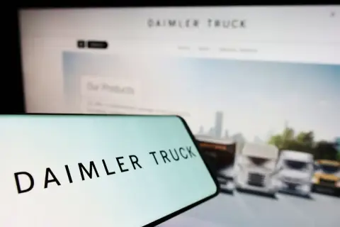 Daimler Truck Logo auf einem Smartphone, im Hintergrund ein Bildschirm mit LKW-Bildern und der Aufschrift "Our Products". Die Daimler Truck Aktie Kurs Prognose im Fokus.