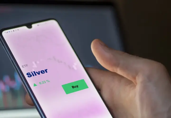 Hand hält Smartphone mit ETF Silber Kursanzeige. Ein grüner "Buy"-Button ist sichtbar, daneben ein Pfeil nach oben und 0,23 %.