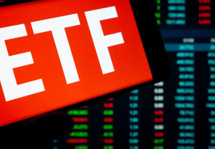 Ein Smartphone zeigt "ETF" auf rotem Grund. Im Hintergrund sind Börsenkurse zu sehen. Ein ETF steuerfrei nach 10 Jahren ist ein Traumziel für Anleger.