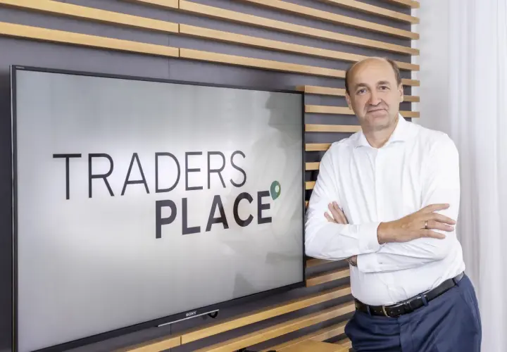 Mann steht vor Bildschirm mit "TRADERS PLACE" Schriftzug.