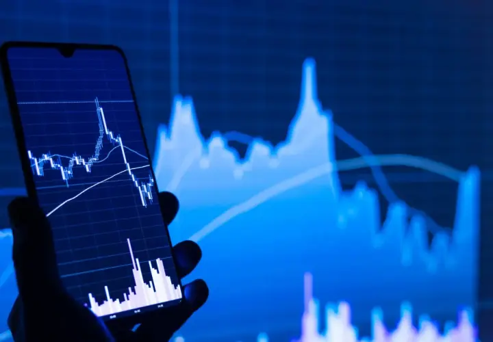 Ein Handy zeigt einen Börsenchart, während im Hintergrund ein größerer Chart zu sehen ist. Ein STP Broker ermöglicht den direkten Marktzugang.