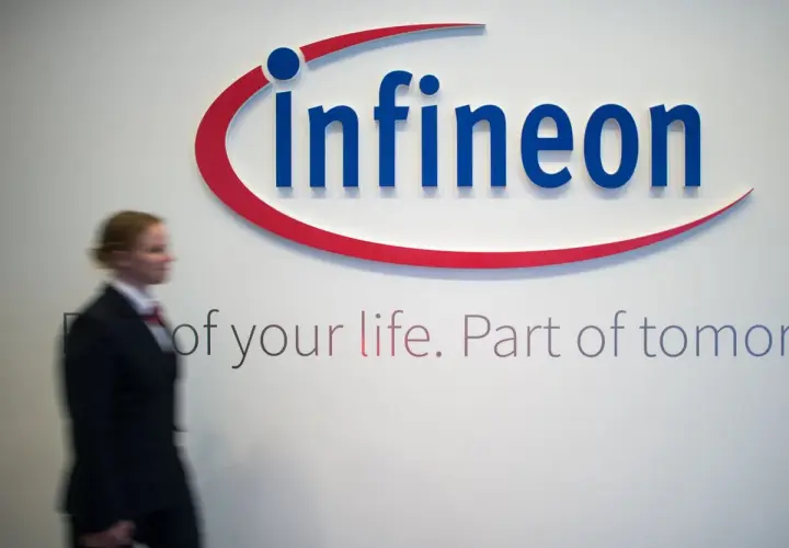Frau im Anzug geht an Infineon-Logo vorbei. Die Infineon-Aktie Prognose ist ein Thema für Investoren.