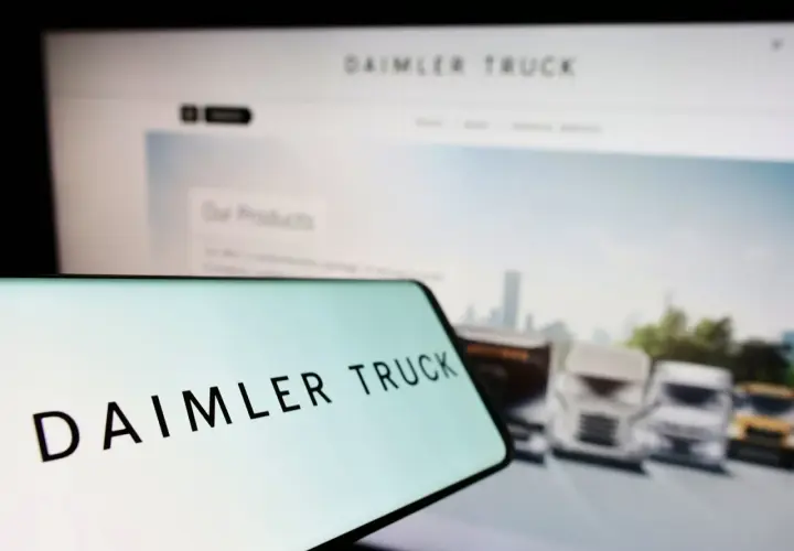 Daimler Truck Logo auf einem Smartphone, im Hintergrund ein Bildschirm mit LKW-Bildern und der Aufschrift "Our Products". Die Daimler Truck Aktie Kurs Prognose im Fokus.