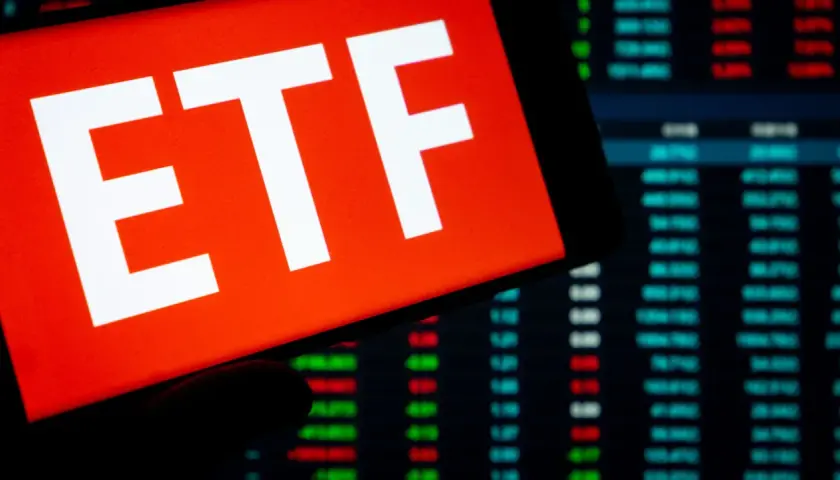 Ein Smartphone zeigt "ETF" auf rotem Grund. Im Hintergrund sind Börsenkurse zu sehen. Ein ETF steuerfrei nach 10 Jahren ist ein Traumziel für Anleger.