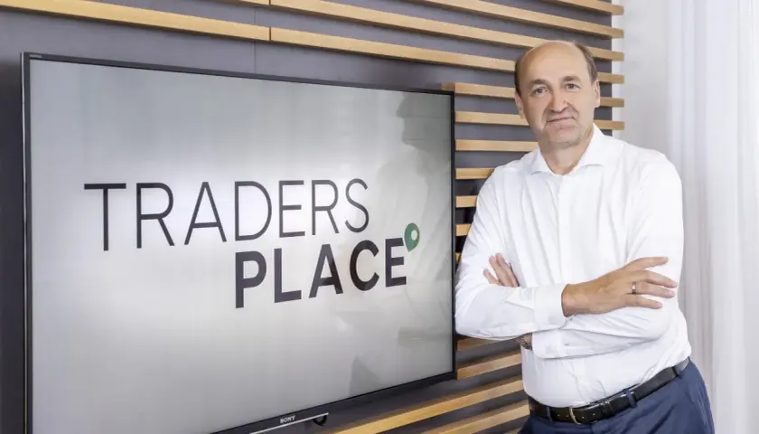 Mann steht vor Bildschirm mit "TRADERS PLACE" Schriftzug.