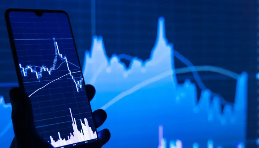Ein Handy zeigt einen Börsenchart, während im Hintergrund ein größerer Chart zu sehen ist. Ein STP Broker ermöglicht den direkten Marktzugang.