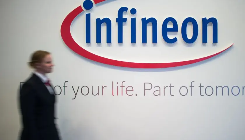 Frau im Anzug geht an Infineon-Logo vorbei. Die Infineon-Aktie Prognose ist ein Thema für Investoren.