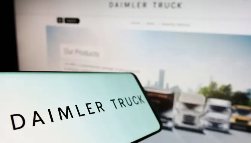 Daimler Truck Logo auf einem Smartphone, im Hintergrund ein Bildschirm mit LKW-Bildern und der Aufschrift "Our Products". Die Daimler Truck Aktie Kurs Prognose im Fokus.