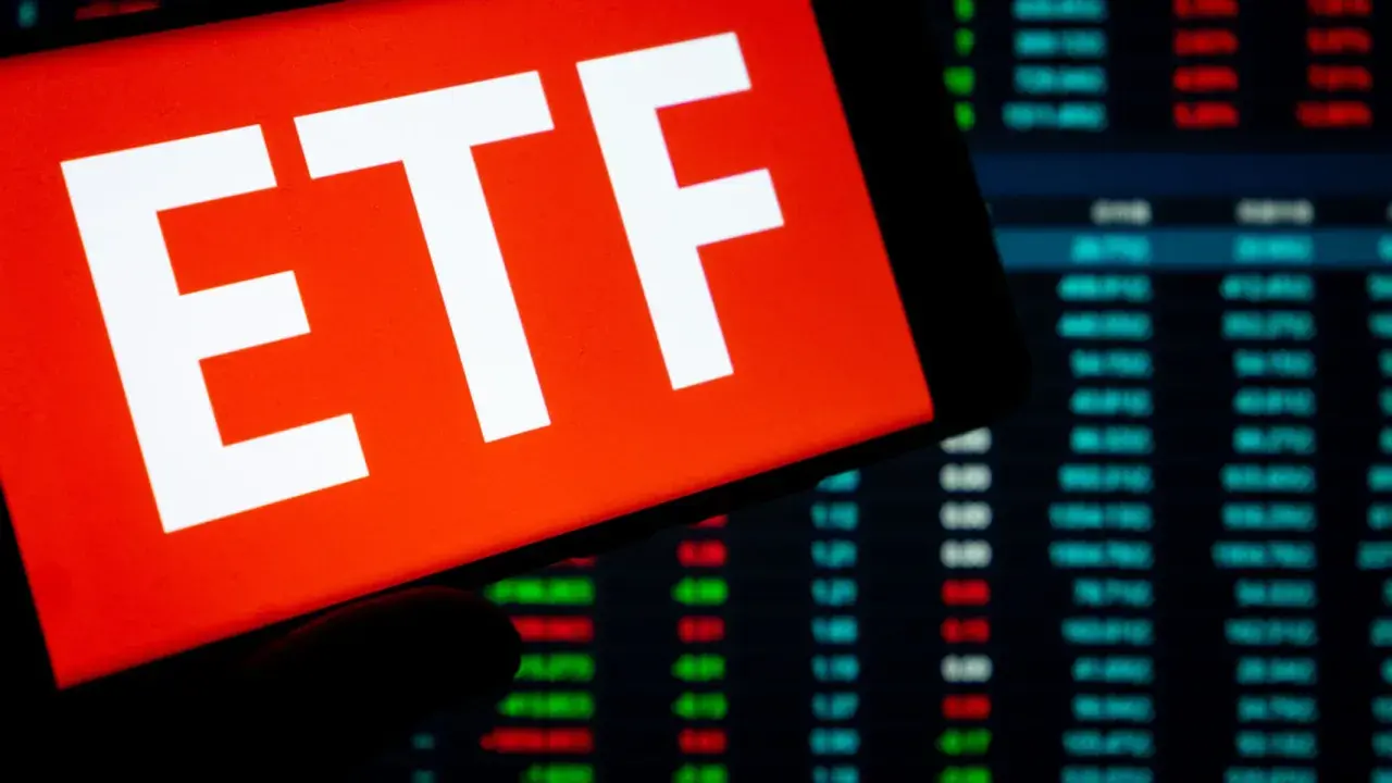 Ein Smartphone zeigt "ETF" auf rotem Grund. Im Hintergrund sind Börsenkurse zu sehen. Ein ETF steuerfrei nach 10 Jahren ist ein Traumziel für Anleger.