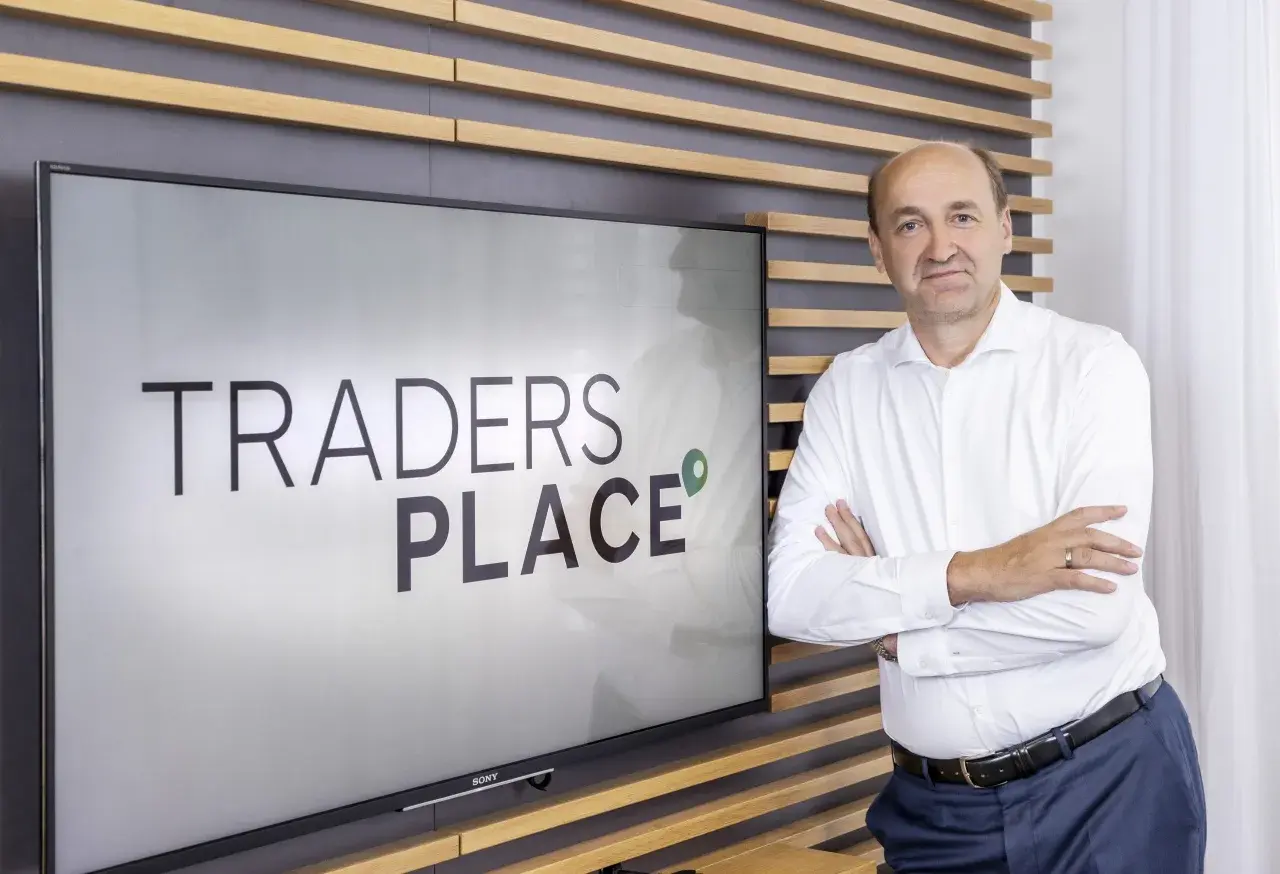 Mann steht vor Bildschirm mit "TRADERS PLACE" Schriftzug.