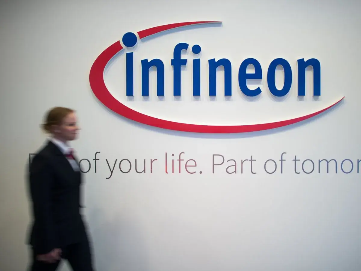 Frau im Anzug geht an Infineon-Logo vorbei. Die Infineon-Aktie Prognose ist ein Thema für Investoren.