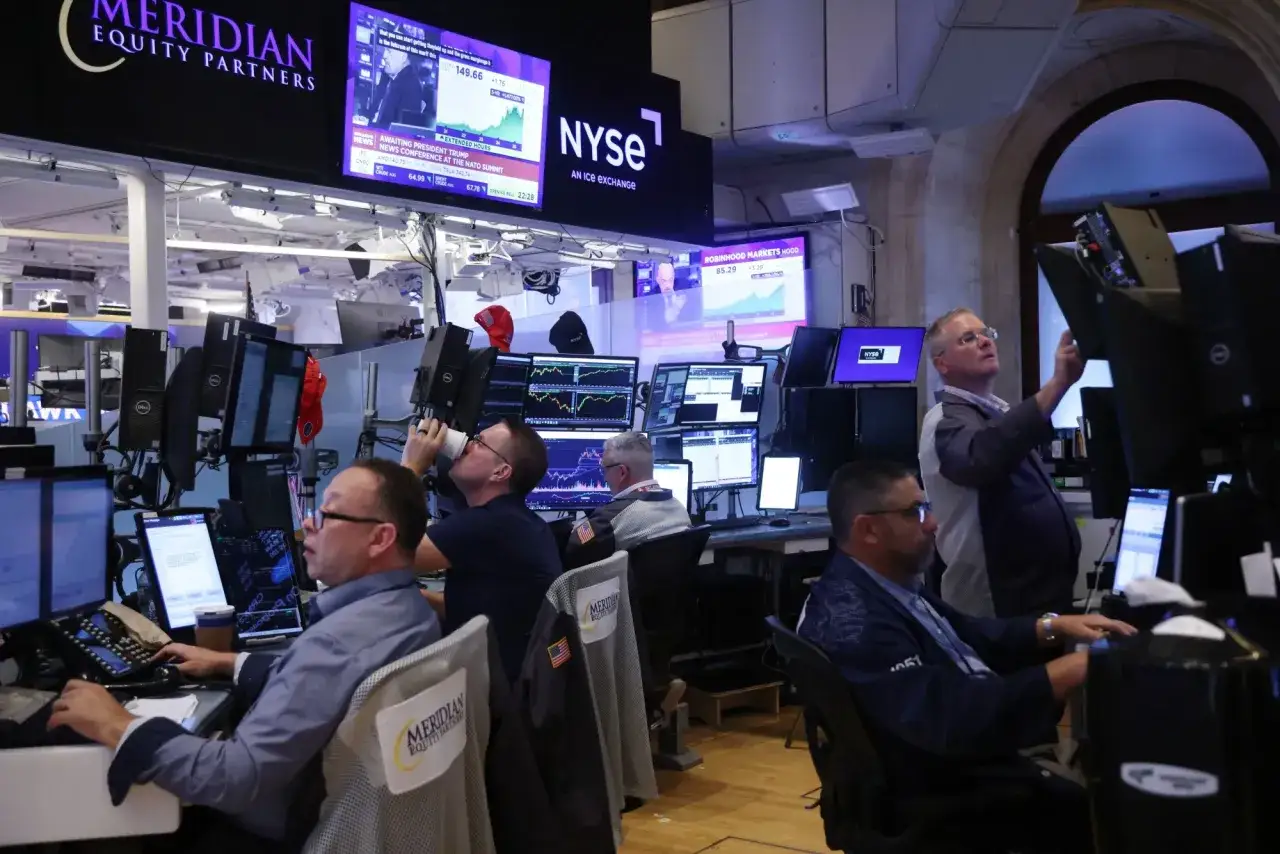 Trader Andrew Hall arbeitet im B&ouml;rsenhandel, umgeben von Bildschirmen mit Aktienkursen und dem NYSE-Logo.